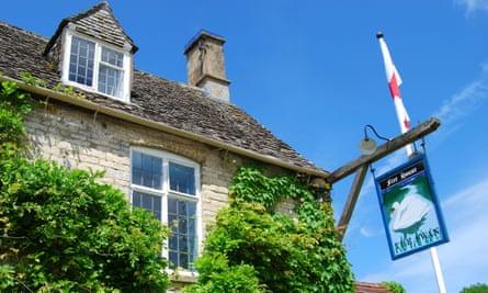 The sign of the Swan Inn, Swinbrook, showing a swan, swinging in front of an ivy-clad stone building